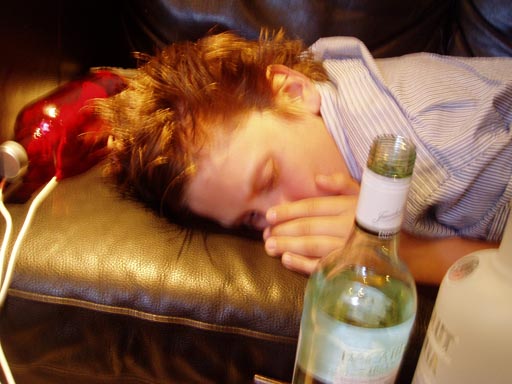 En mörkhårig kille ligger på en soffa, framför honom står en flaska alkohol